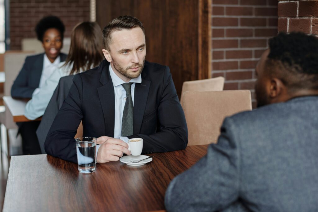 Two businessmen in suits discussing over coffee during a meeting in a café.